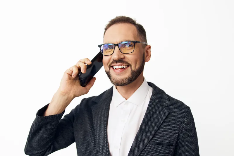 A professional businessman on a clean white background, smiling while talking on a phone. Confident, approachable, and polished, the image conveys success, effective communication, and a modern work