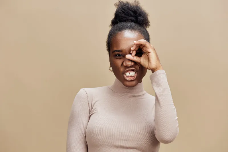 Expressive African woman playfully showcasing a creative gesture with her hand against a neutral beige background, exuding confidence and charisma
