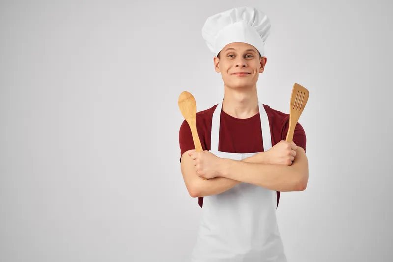 Повар-мужчина в белом фартуке с кухонной утварью готовит изысканную еду