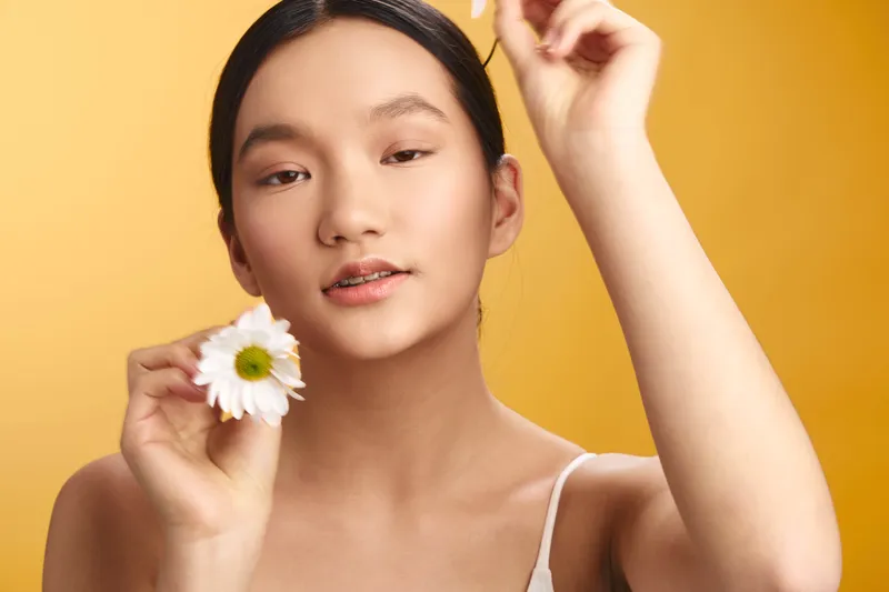 asian woman holds a white flower against a warm backdrop, radiating calm and gentle beauty. her soft expression suggests serenity and grace, creating an intimate, uplifting mood.