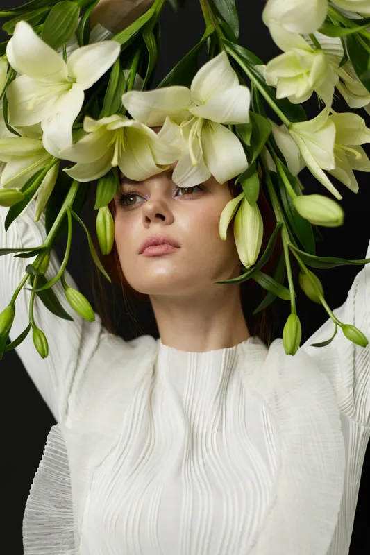 Elegant woman with flowers, showcasing a serene expression and white attire, embodying beauty and nature in a minimalist setting