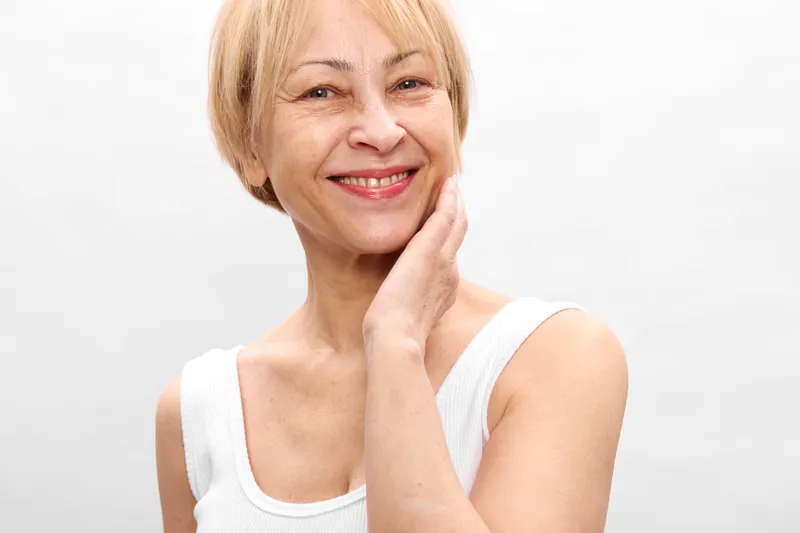Woman portrait, smiling senior, beauty skincare health relaxation mood, hand on cheek gesture, clean white studio background, relaxed facial expression, copy space