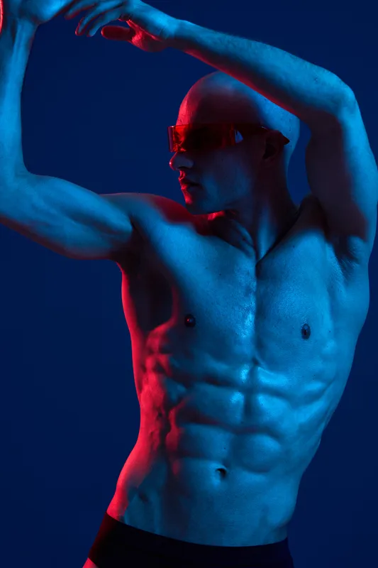 Muscular man posing dramatically under vibrant lighting, showcasing an energetic and modern aesthetic in a striking blue and red color scheme.