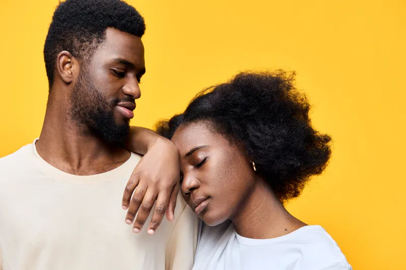 Young Black couple expressing love and affection against a bright yellow background, showcasing emotional connection and intimacy in a stylish and modern setting