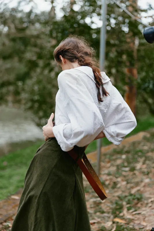 A young woman in a white shirt and green skirt stands outdoors, expressing contemplation with a nature inspired background, symbolizing eco friendliness and simplicity