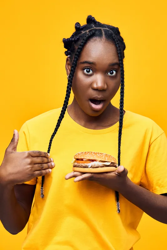 Surprised young woman holding a delicious healthy sandwich, dressed in a bright yellow t shirt against a vivid yellow background, showcasing healthy eating