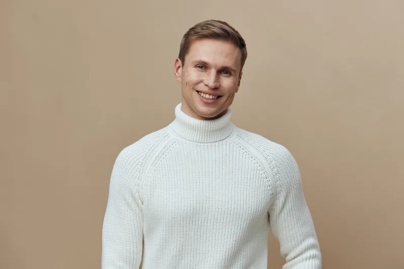 Smiling man wearing white knit turtleneck sweater standing on beige background happy casual lifestyle concept