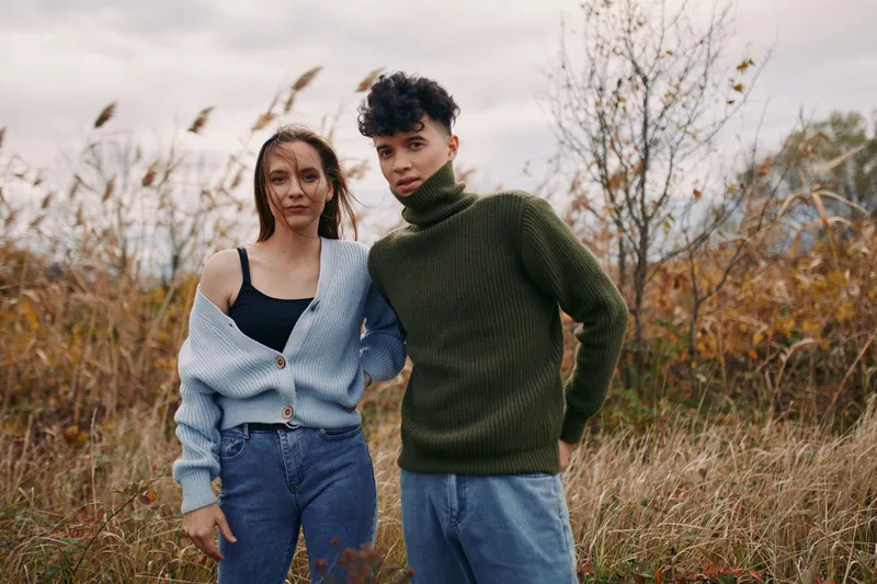 Two individuals share a candid moment in an autumn field under natural light, embracing authenticity with relaxed posture, simple outfits, and genuine expressions amid tall grasses.