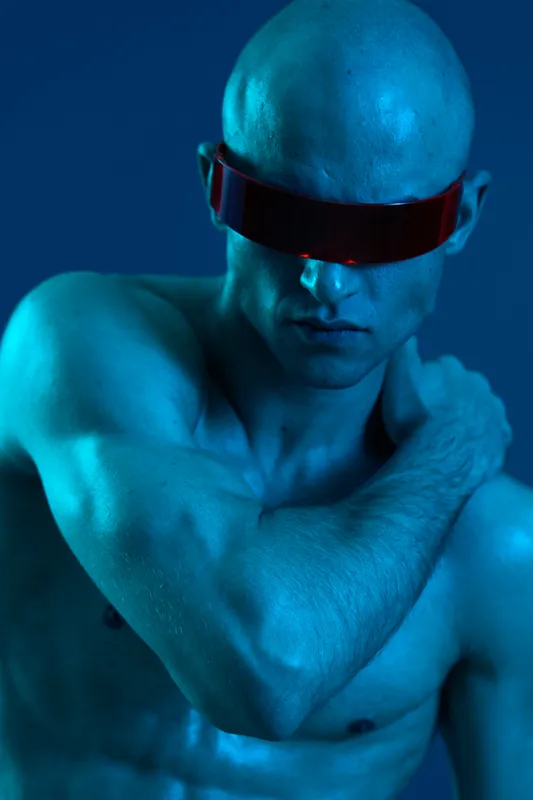 Bold man wearing futuristic sunglasses, showcasing a unique blue tone and striking pose, exuding confidence and modern vibes in an artistic, captivating setting.