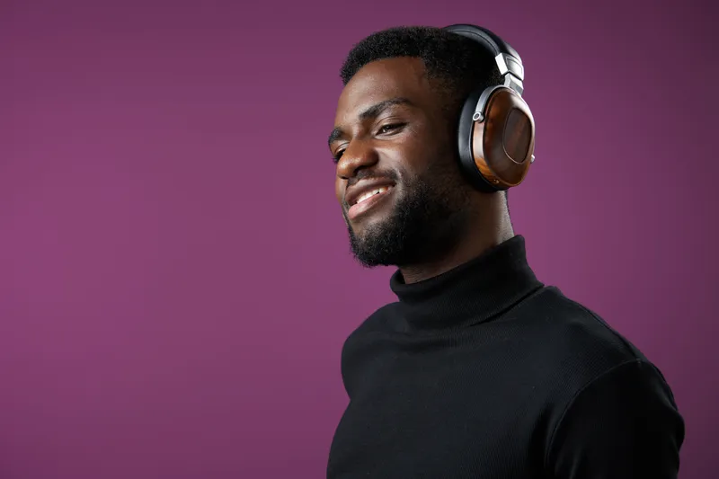 Smiling young Black man wearing headphones against a vibrant purple background, expressing joy and relaxation with modern style