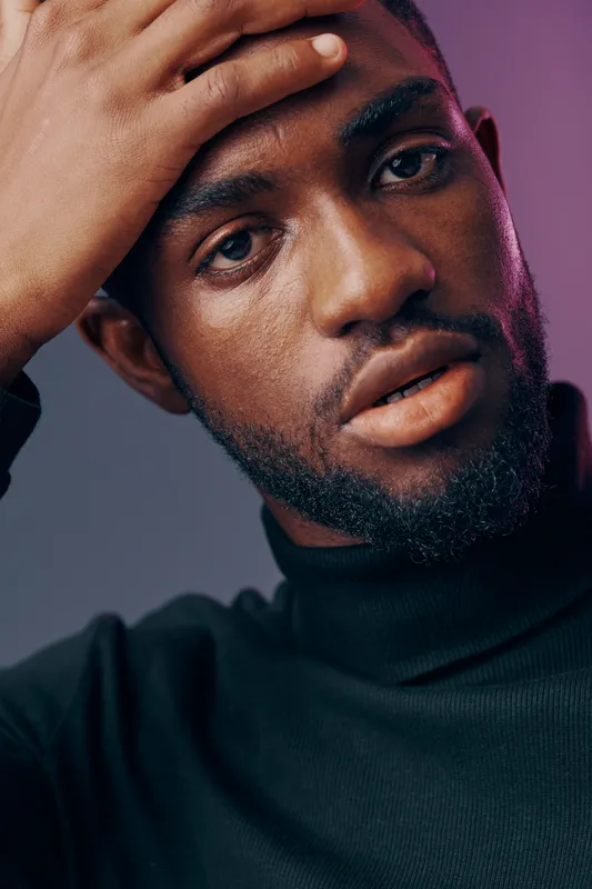 Close up portrait of a Black male model with a serious expression, wearing a black turtleneck, highlighting modern fashion trends and masculine elegance