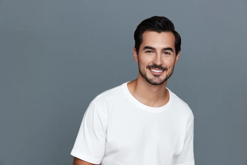 Smiling man wearing a white t-shirt stands against a grey background, exuding confidence and warmth in a cheerful studio portrait. People lifestyle concept.