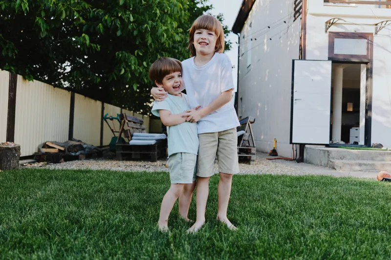 Two cheerful boys playing together in a sunny backyard, capturing the essence of childhood joy and sibling bond in a vibrant green setting.