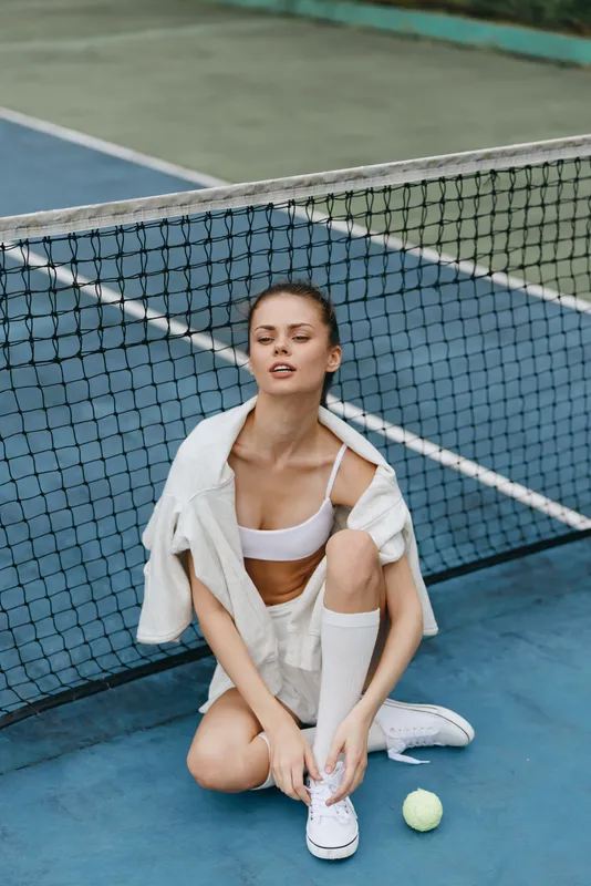 Young athletic woman in sporty outfit posing confidently on tennis court, showcasing fitness, determination, and a healthy lifestyle