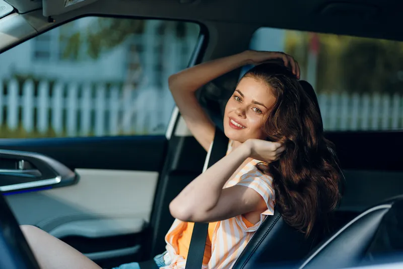 Жизнерадостная молодая женщина наслаждается беззаботным моментом в своем автомобиле, естественный солнечный свет освещает ее лицо