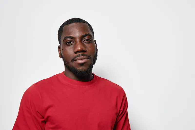 African american man with dark skin wearing red sweater looking at camera with confident expression on white background in studio portrait.