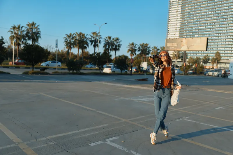 Young woman with skateboard in urban parkinglot by palm trees at sunset, casual smile and jeans capturing candid lifestyle, authenticity and golden hour glow, mindful living and emotional