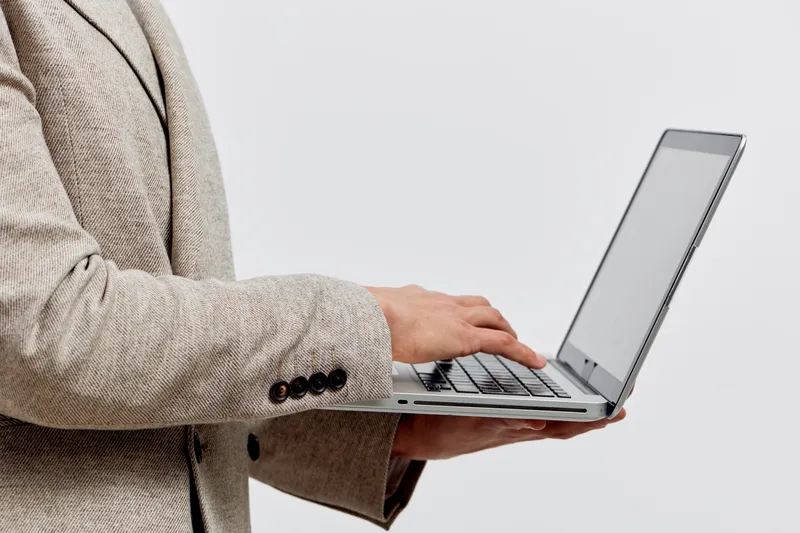 man holding laptop using technology typing on keyboard wearing beige jacket isolated on white background digital nomad concept