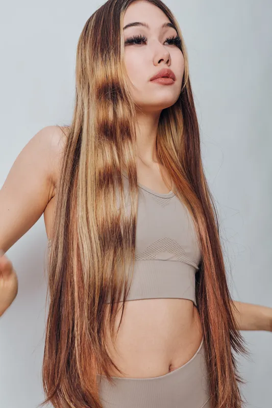 Young woman with long straight hair and natural makeup posing against light background in stylish outfit showcasing modern beauty and confidence.
