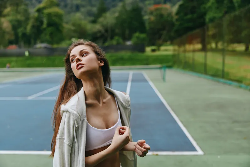 Young woman exercising on an outdoor tennis court, wearing a sports bra and hoodie, showing confidence and determination in an active lifestyle