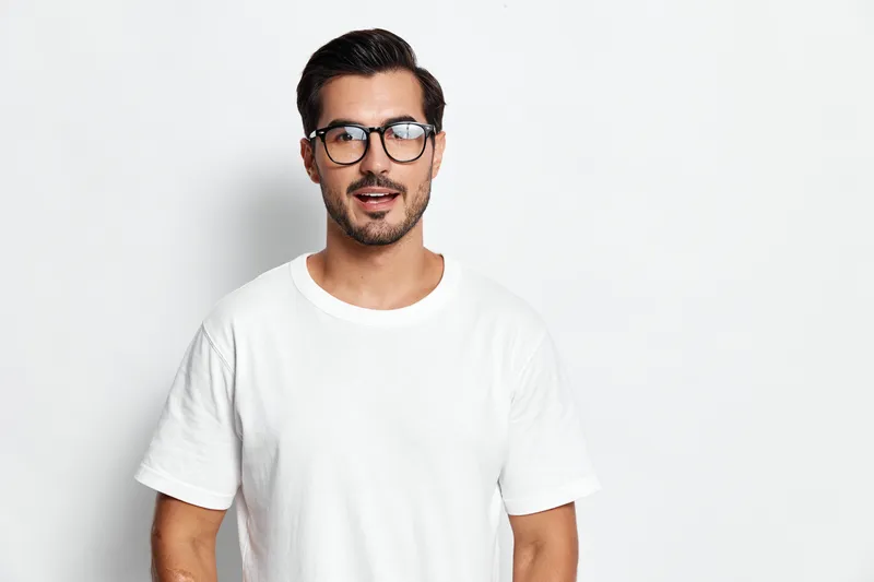 Full body smiling young man wear casual white t-shirt and glasses look at camera with amazed expression, isolated on light solid background. Lifestyle concept.