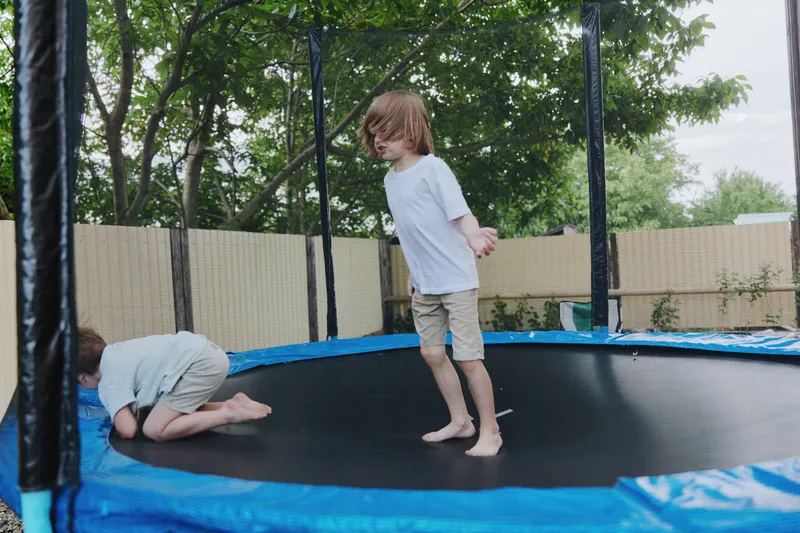 Joyful children jumping on a trampoline, capturing the essence of childhood energy and playfulness amidst lush greenery and bright summer sunlight.