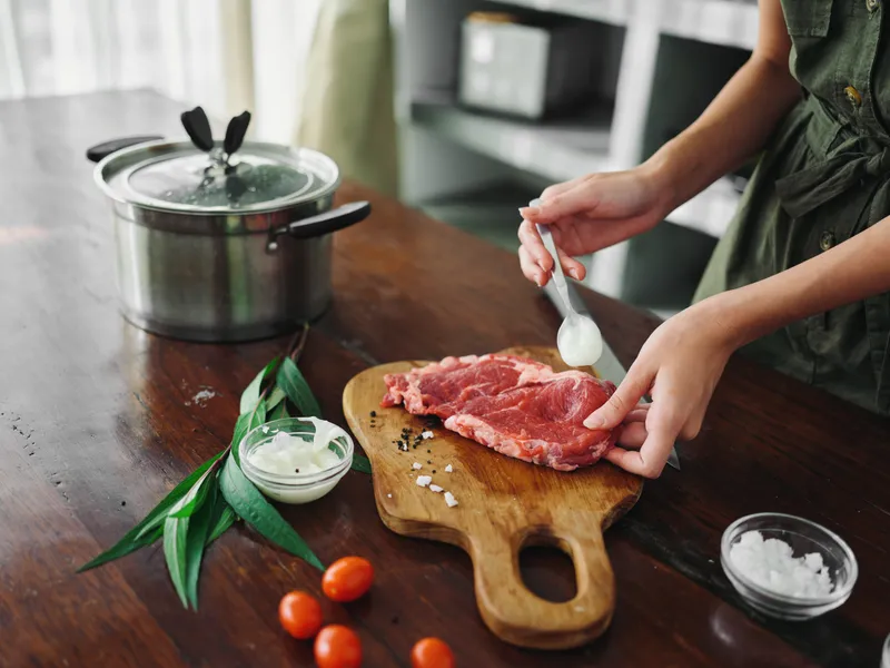 На кухне женщина готовит ужин из мяса, овощей и специй на деревянном столе на фоне стильной кухни, крупным планом руки, свежие экологичные продукты, образ жизни