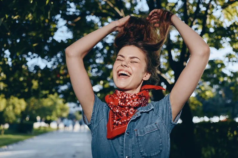 joyful woman in modern boho-western denim outfit with a red bandana, laughing outdoors in natural light, lifestyle street style with film color effect