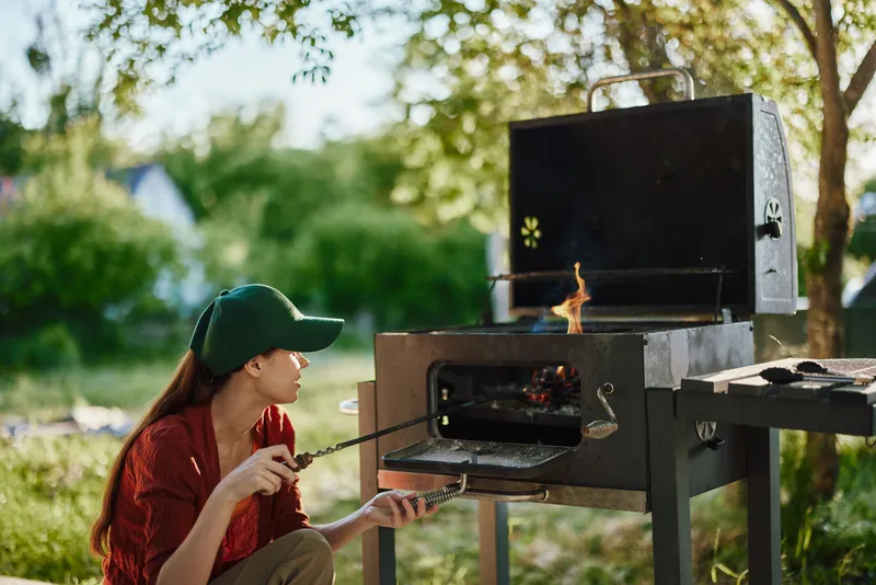 Young woman grilling outdoors in a green park, showcasing summer cooking vibes with vibrant colors and a joyful atmosphere