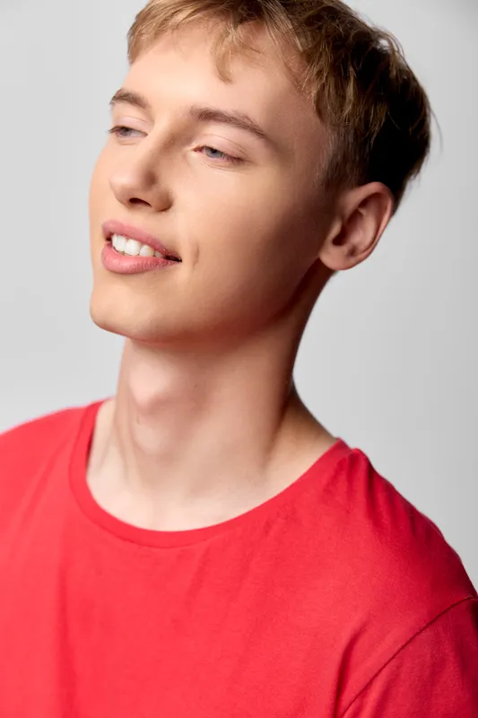 Smiling young man wearing a red shirt with a cheerful expression, casual style and warm lighting for lifestyle and fashion context, showcasing a relaxed pose and natural mood in a clean studio setting