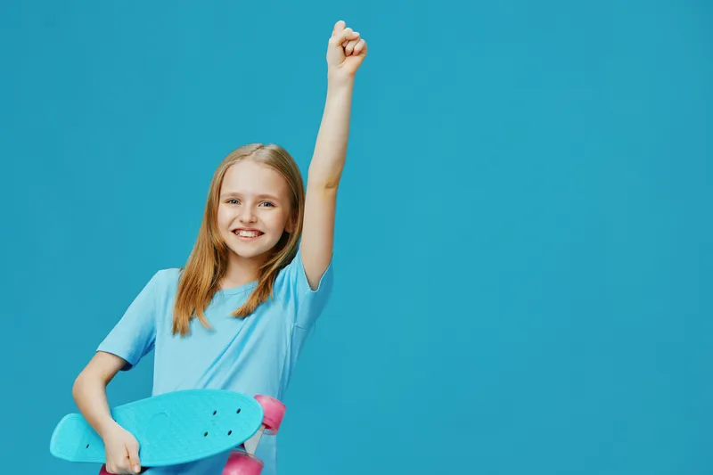 Joyful girl celebrating her victory with a skateboard against a bright blue background, embodying youth and energy