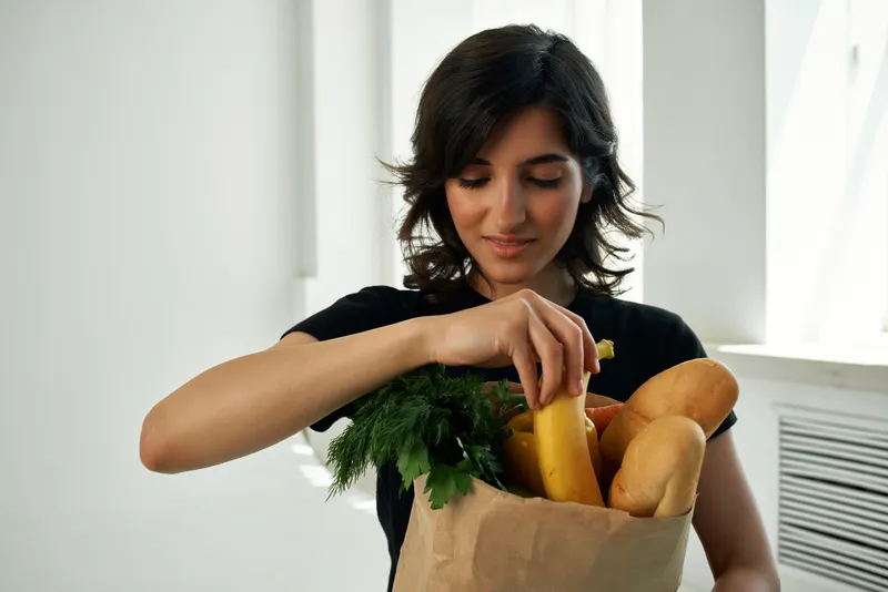 Женщина в черной футболке с пакетом продуктов: овощи, фрукты, здоровая еда