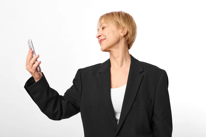 Woman in business suit holding smartphone, smiling in studio profile, communication concept, professional adult portrait, modern work life, white background