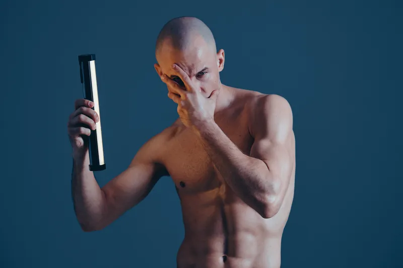 Strong man posing with a light, showcasing emotions in a dramatic black and white composition. Capturing the essence of strength and vulnerability in a creative manner.