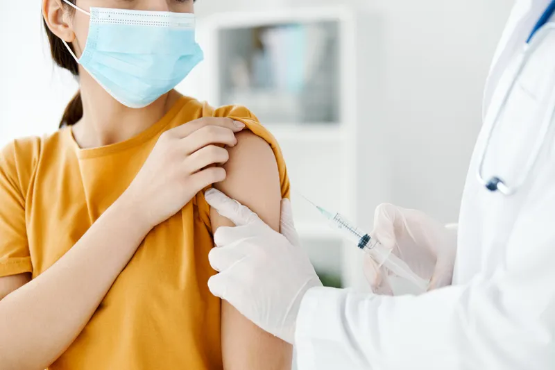 Вид сбоку: врач делает инъекцию вакцины в плечо пациента в медицинской маске