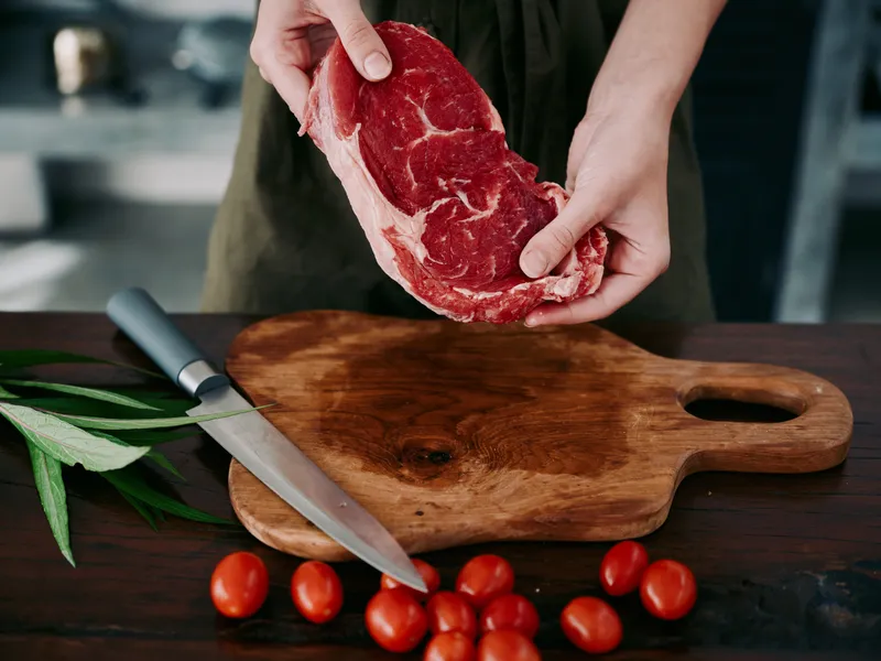 Женщина с ножом в руке нарезает свежее мясо стейка для жарки на кухне