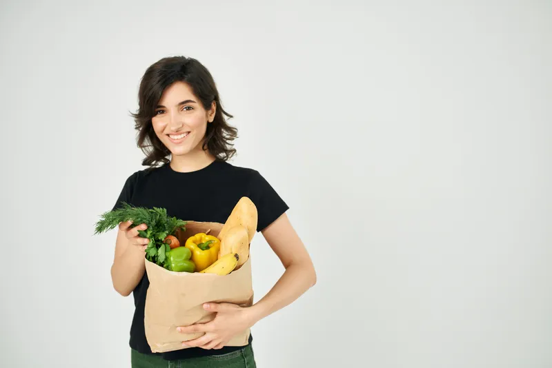 Симпатичная женщина с пакетом продуктов, здоровое питание, овощи, светлый фон