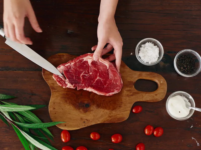 Женщина с ножом в руке нарезает свежее мясо для жарки на кухне