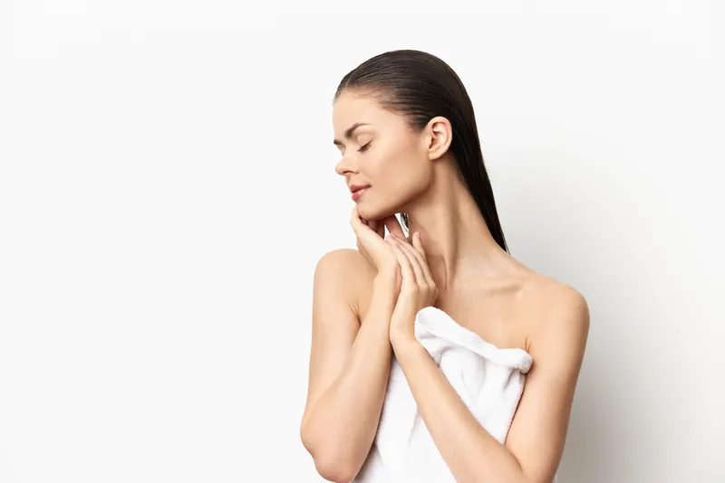 Безмятежный портрет женщины с длинными мокрыми волосами, которая нежно касается лица, завернувшись в белое полотенце