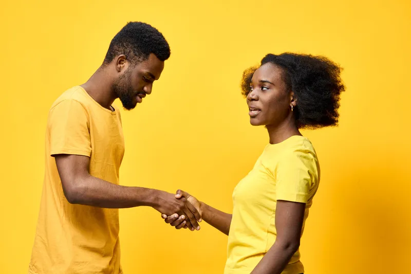 Young African couple shaking hands in matching yellow attire against a vibrant yellow background, symbolizing unity and collaboration in friendship or business