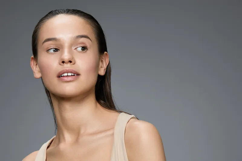 Serene portrait of a young Asian woman with natural makeup, gazing over her shoulder against a soft gray background, exuding confidence and grace