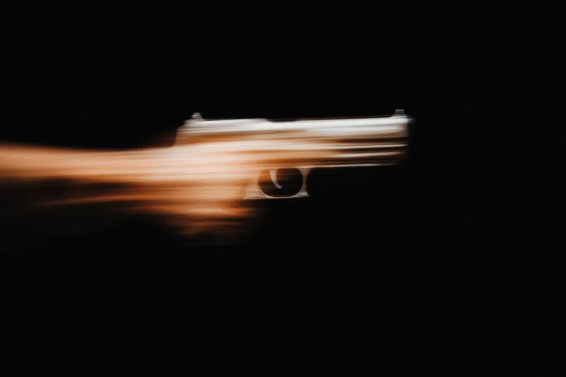 Динамичное размытие в движении пистолета вызывает чувство срочности и опасности, иллюстрируя темы действия и напряженности на резком черном фоне