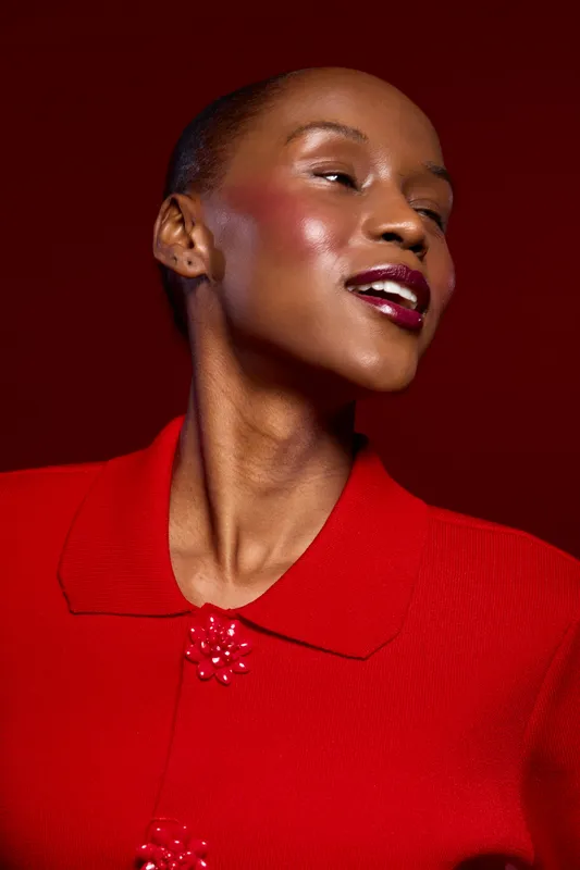 Elegant dark skinned African woman in red outfit poses with closed eyes and bright lipstick on dark red background. Concept of beauty, fashion, confidence, and glamour.
