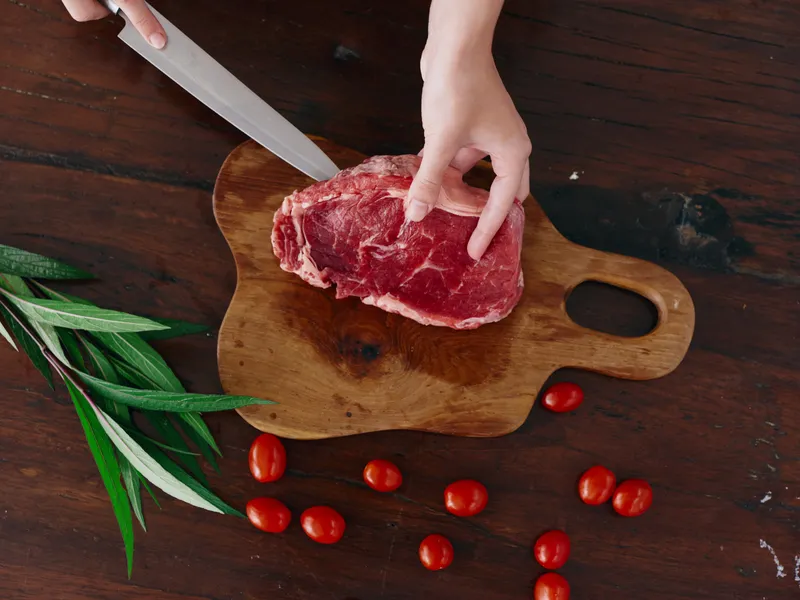 Женщина с ножом в руке нарезает свежее стейковое мясо для жарки на кухне