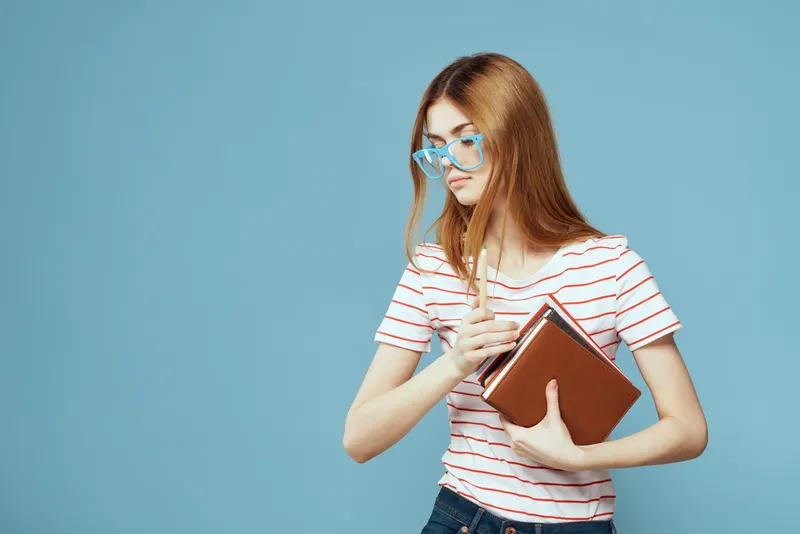 Студентка с книгами в руках на голубом фоне, в жёлтых очках, модельная причёска, кадрированный вид