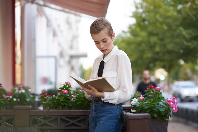 Студент с книгой в руках отдыхает на летней террасе кафе