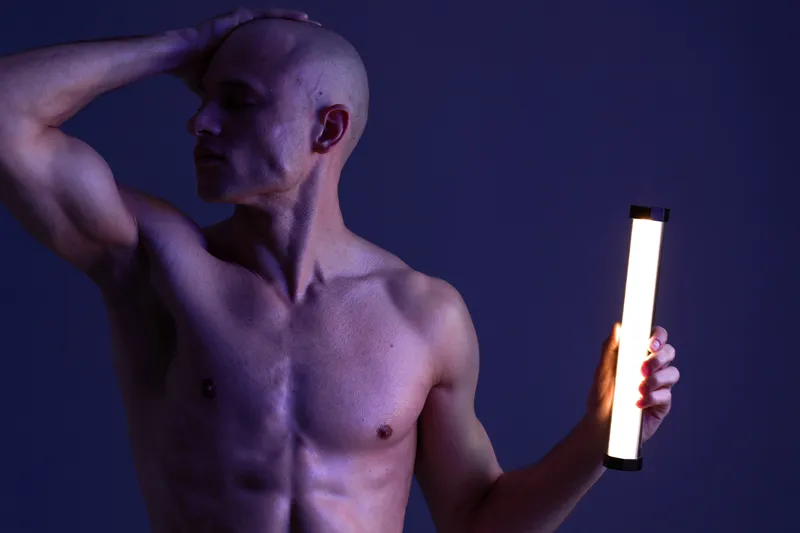 Muscular man posing with light in a dark setting, showcasing contrast and dynamic shadowing. The image emphasizes strength and form through creative lighting techniques.