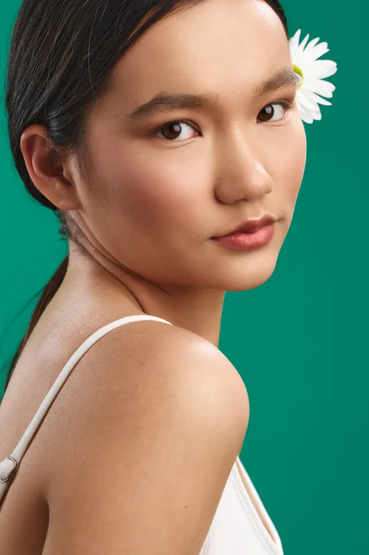 asian woman with a white flower in her hair, close up portrait under studio lighting against a green backdrop, calm expression conveying elegance and poise.