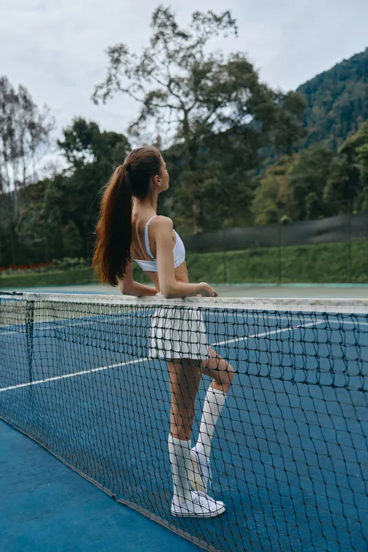 Young female tennis player in stylish athletic wear enjoying a moment on the court, showcasing emotions of confidence and determination, set against a serene outdoor backdrop