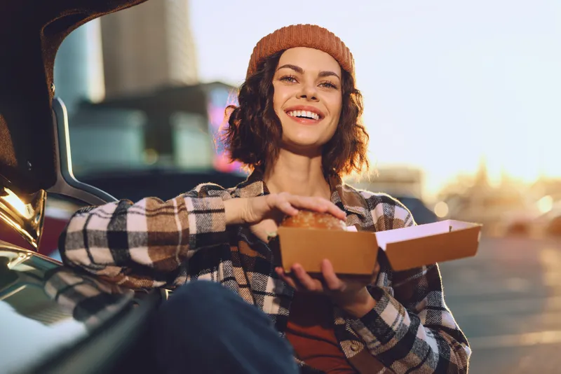 Woman smile takeout car golden hour candid urban scene of a joyful woman enjoying takeout by a trunk at sunset, authenticity and mindful lifestyle, emotional storytelling and warm glow.